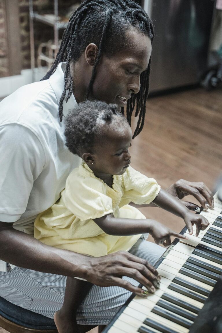 A father and his young daughter bond over playing the piano indoors.