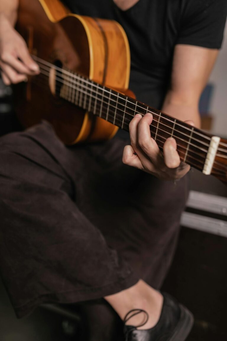 An adult man strums an acoustic guitar indoors, focusing on musical expression.